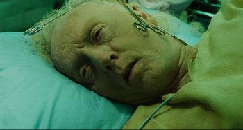 Movie still from “Saw III” (2006), directed by Darren Lynn Bousman – An older man laying in a hospital bed with a pair of scissors; Close Up shot, Overhead angle