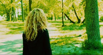 Movie still from “Saw III” (2006), directed by Darren Lynn Bousman – A woman standing in a park looking out at the trees; Medium shot, Over the shoulder angle