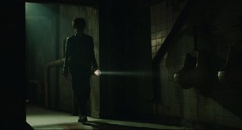 Movie still from “Saw III” (2006), directed by Darren Lynn Bousman – A person with a flashlight walking in a dark room; Wide shot, Low angle