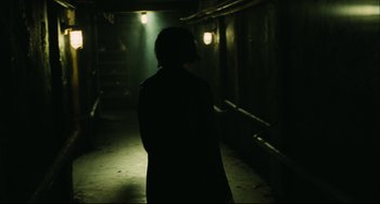Movie still from “Saw III” (2006), directed by Darren Lynn Bousman – A person walking down a dark path in a building; Wide shot, Over the shoulder angle