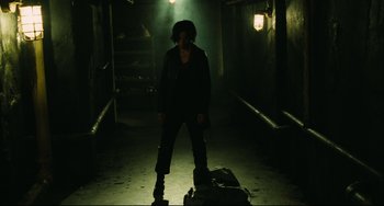 Movie still from “Saw III” (2006), directed by Darren Lynn Bousman – A person standing in a dark room with a suitcase; Wide shot, Low angle