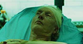 Movie still from “Saw III” (2006), directed by Darren Lynn Bousman – An older man with a bandaged head rests in a hospital bed; Close Up shot, Low angle