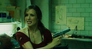 Movie still from “Saw III” (2006), directed by Darren Lynn Bousman – A woman holding a gun in a room with a brick wall; Close Up shot, Over the shoulder angle