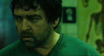 Movie still from “Saw III” (2006), directed by Darren Lynn Bousman – A person with a green shirt on; Close Up shot, Over the shoulder angle
