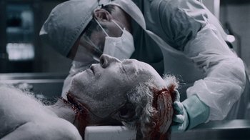 Movie still from “Saw IV” (2007), directed by Darren Lynn Bousman – A man with a head wound is being examined by a doctor; Close Up shot, Over the shoulder angle