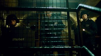 Movie still from “Saw IV” (2007), directed by Darren Lynn Bousman – A man standing inside of a jail cell behind bars; Medium shot, Low angle
