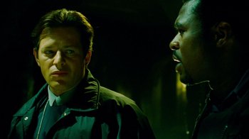 Movie still from “Saw IV” (2007), directed by Darren Lynn Bousman – A man and a man standing next to each other in the dark; Close Up shot, Over the shoulder angle