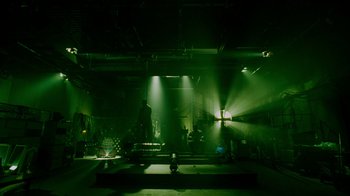 Movie still from “Saw IV” (2007), directed by Darren Lynn Bousman – A stage lit up with green lights in a dark room; Extreme Wide shot, Low angle
