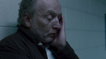 Movie still from “Saw IV” (2007), directed by Darren Lynn Bousman – An older man sitting in front of a brick wall with his hand on his face; Close Up shot, High angle