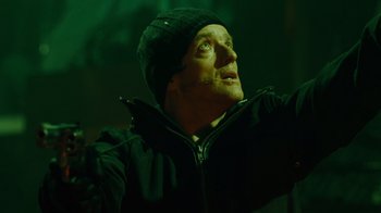 Movie still from “Saw IV” (2007), directed by Darren Lynn Bousman – A man in a black jacket and a black hat looking up; Close Up shot, Low angle