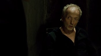 Movie still from “Saw IV” (2007), directed by Darren Lynn Bousman – An older man sitting in a chair in a dark room; Close Up shot, Over the shoulder angle