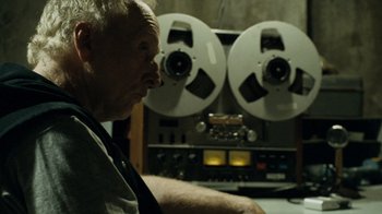 Movie still from “Saw IV” (2007), directed by Darren Lynn Bousman – An older man sitting in front of an audio tape recorder; Close Up shot, Low angle