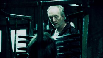 Movie still from “Saw IV” (2007), directed by Darren Lynn Bousman – An older man standing in front of a machine; Medium shot, Over the shoulder angle