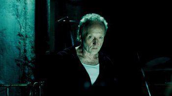 Movie still from “Saw IV” (2007), directed by Darren Lynn Bousman – An older man is standing in a dark room; Close Up shot, Over the shoulder angle