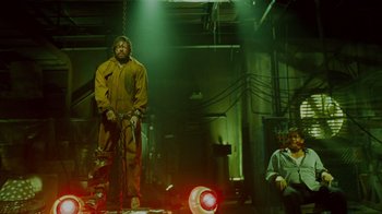 Movie still from “Saw IV” (2007), directed by Darren Lynn Bousman – A man standing in a room holding a chainsaw; Wide shot, Low angle