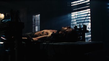 Movie still from “Saw V” (2008), directed by David Hackl – A shirtless man laying on a bed in a room; Wide shot, Low angle