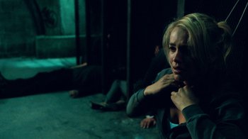 Movie still from “Saw V” (2008), directed by David Hackl – A woman is sitting on the ground in a dark room; Medium shot, Over the shoulder angle