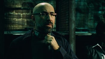 Movie still from “Saw V” (2008), directed by David Hackl – A bald man with glasses and a beard is wearing glasses; Close Up shot, Low angle