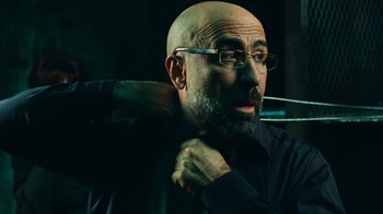 Movie still from “Saw V” (2008), directed by David Hackl – A bald man with glasses holding a baseball bat in his hands; Close Up shot, Low angle