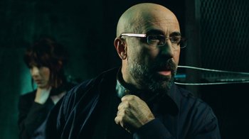 Movie still from “Saw V” (2008), directed by David Hackl – A bald man with glasses and a beard is adjusting his tie; Close Up shot, Over the shoulder angle