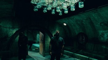 Movie still from “Saw V” (2008), directed by David Hackl – A man standing in a dark room under a light fixture; Wide shot, Low angle