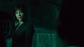 Movie still from “Saw V” (2008), directed by David Hackl – A woman in a black suit standing next to a wall; Medium shot, Over the shoulder angle