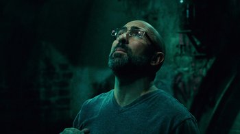 Movie still from “Saw V” (2008), directed by David Hackl – A man with a goatee wearing glasses looking up; Close Up shot, Low angle
