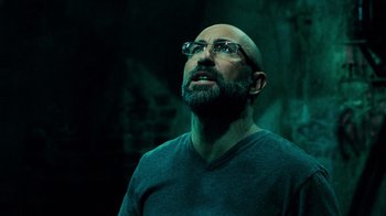 Movie still from “Saw V” (2008), directed by David Hackl – A man with a beard wearing glasses and a gray t - shirt; Close Up shot, Low angle