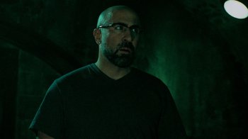 Movie still from “Saw V” (2008), directed by David Hackl – A man with a bald head wearing glasses and a black t - shirt; Close Up shot, Low angle