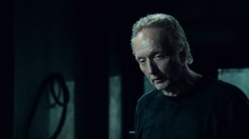 Movie still from “Saw V” (2008), directed by David Hackl – An older man in a black shirt is looking at the camera; Close Up shot, Over the shoulder angle