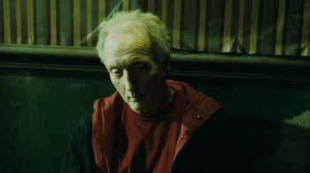 Movie still from “Saw V” (2008), directed by David Hackl – An old man with a red shirt is sitting on a bench; Close Up shot, High angle