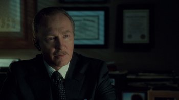 Movie still from “Saw V” (2008), directed by David Hackl – A man in a suit and tie in front of a picture; Close Up shot, Low angle