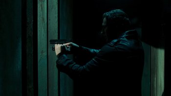 Movie still from “Saw V” (2008), directed by David Hackl – A man in a black jacket is holding a gun; Medium shot, Over the shoulder angle