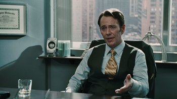 Movie still from “Saw VI” (2009), directed by Kevin Greutert – A man sitting at a desk in a suit and tie; Medium shot, Over the shoulder angle