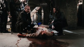 Movie still from “Saw VI” (2009), directed by Kevin Greutert – A group of people standing around a body covered in fake blood; Wide shot, Over the shoulder angle