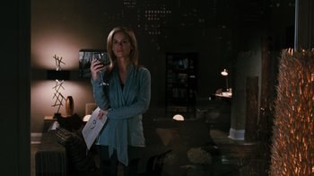 Movie still from “Saw VI” (2009), directed by Kevin Greutert – A woman holding a wine glass in a dark room; Medium shot, Over the shoulder angle