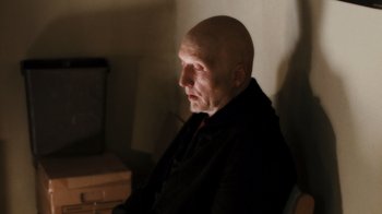 Movie still from “Saw VI” (2009), directed by Kevin Greutert – An older bald man sitting in front of a wall; Close Up shot, Over the shoulder angle