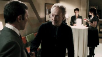Movie still from “Saw VI” (2009), directed by Kevin Greutert – A man shaking hands with another man in front of a table; Medium shot, Over the shoulder angle