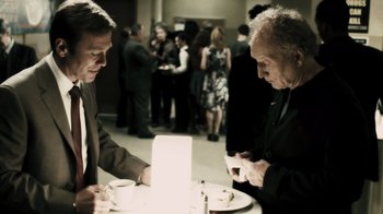 Movie still from “Saw VI” (2009), directed by Kevin Greutert – Two men sitting at a table with cups of coffee; Medium shot, Over the shoulder angle