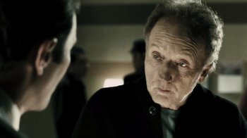 Movie still from “Saw VI” (2009), directed by Kevin Greutert – An older man wearing a black jacket and a green neck tie; Close Up shot, Over the shoulder angle