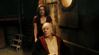 Movie still from “Saw VI” (2009), directed by Kevin Greutert – A woman standing next to an older man in a room; Medium shot, High angle