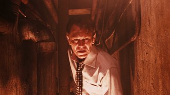 Movie still from “Saw VI” (2009), directed by Kevin Greutert – A man wearing a neck tie standing in a room; Medium shot, Low angle