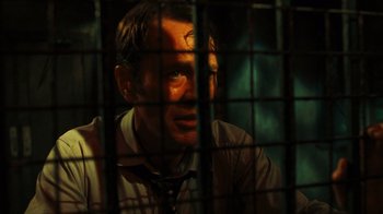 Movie still from “Saw VI” (2009), directed by Kevin Greutert – A man sitting in front of a metal fence; Close Up shot, Low angle