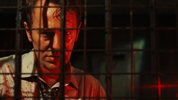 Movie still from “Saw VI” (2009), directed by Kevin Greutert – A man in a red shirt behind a metal fence; Close Up shot, Low angle