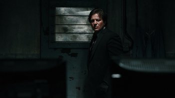 Movie still from “Saw VI” (2009), directed by Kevin Greutert – A man in a suit and tie standing in a dark room; Medium shot, Low angle