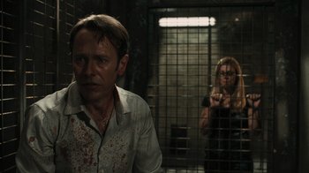 Movie still from “Saw VI” (2009), directed by Kevin Greutert – A man and a woman standing in front of each other in a jail cell; Medium shot, Over the shoulder angle