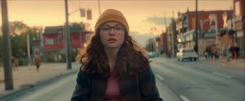Movie still from “Scary Stories to Tell in the Dark” (2019), directed by André Øvredal – A woman wearing glasses and a hat standing on the side of the road; Medium shot, Over the shoulder angle