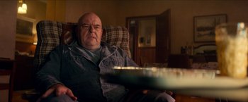 Movie still from “Scary Stories to Tell in the Dark” (2019), directed by André Øvredal – An older man sitting in a chair holding a tray of food; Medium shot, Over the shoulder angle