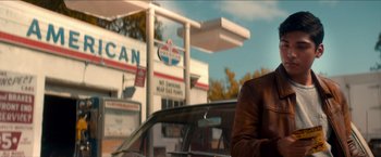 Movie still from “Scary Stories to Tell in the Dark” (2019), directed by André Øvredal – A man sitting in the drivers seat of a car in front of an american gas station; Medium shot, Over the shoulder angle