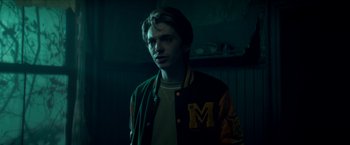 Movie still from “Scary Stories to Tell in the Dark” (2019), directed by André Øvredal – A man in a green and yellow jacket standing in a dark room; Medium shot, Over the shoulder angle